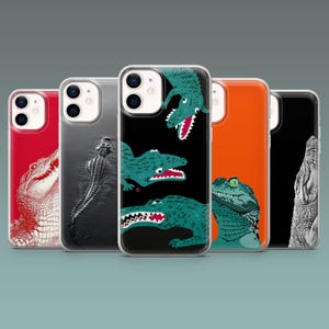 Könnte beinhalten: Eine Auswahl an Handyhüllen mit Alligator- und Krokodil-Designs. Die Hüllen zeigen verschiedene Illustrationen, darunter ein rot-weißer Alligatorkopf, ein Graustufen-Krokodil und grüne Krokodile auf schwarzem und orangefarbenem Hintergrund.