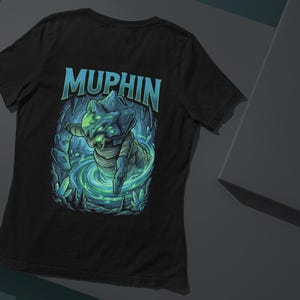 Könnte beinhalten: Schwarzes T-Shirt mit einer detaillierten Illustration einer Kreatur, die aus einer wirbelnden, leuchtenden blau-grünen Umgebung auftaucht. Das Wort "MUPHIN" ist in einer stilisierten Schriftart über der Kreatur gedruckt.