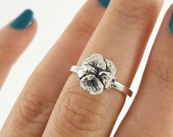 May include: A silver ring with a flower design. The ring is on a finger with teal nail polish.