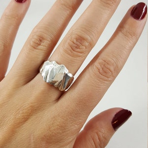 May include: A silver ring with a textured, wavy design. The ring is worn on a finger with dark red nail polish.