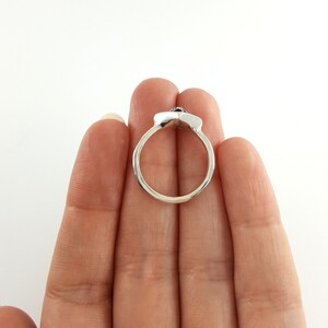 May include: A silver ring with a black stone set in the center. The ring is shown on a hand, but the hand is not visible in the image.