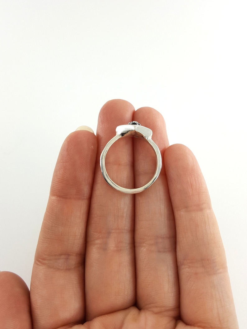 May include: A silver ring with a black stone set in the center. The ring is shown on a hand, but the hand is not visible in the image.