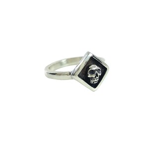 May include: A silver ring with a diamond-shaped setting featuring a small skull design.