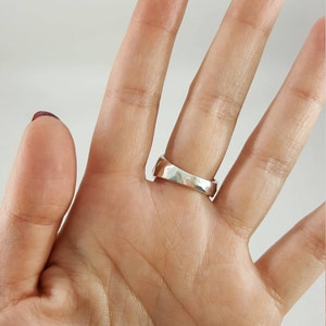 May include: A silver ring with a textured, hammered finish. The ring is worn on the middle finger of a hand.
