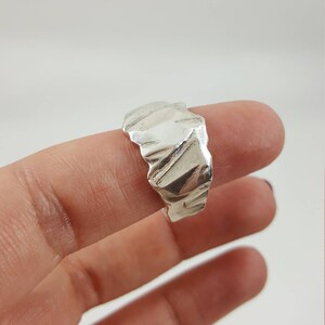 May include: A silver ring with a textured, organic design. The ring is worn on a finger.