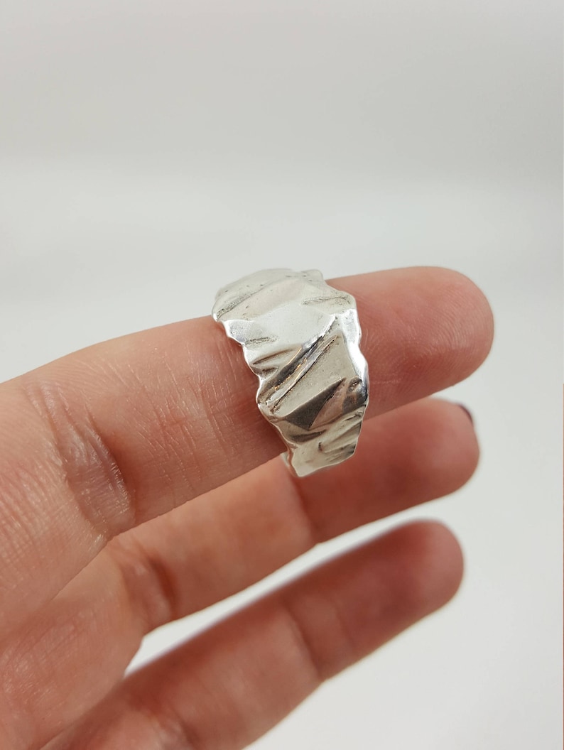 May include: A silver ring with a textured, organic design. The ring is worn on a finger.