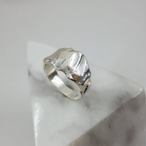 May include: A silver ring with a textured, organic design. The ring is made of metal and has a unique, modern style.