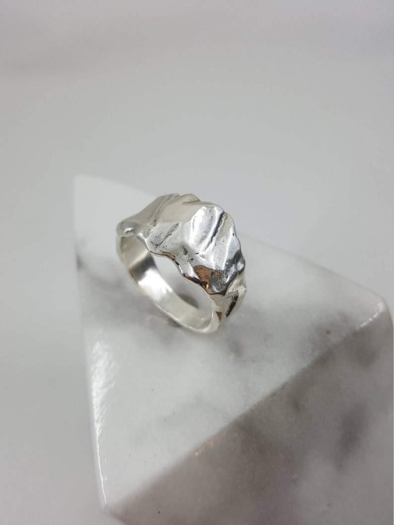 May include: A silver ring with a textured, organic design. The ring is made of metal and has a unique, modern style.