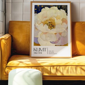 May include: A framed art print featuring a large, pale yellow and white flower with a dark blue background. The text KLIMT 1862-1918, ROMA, 1891, VER SACRUM, and WIENER SECESSION is printed in black at the bottom of the white border within the frame.
