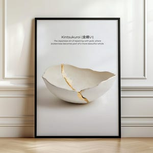 May include: A framed wall art print featuring a white, irregularly shaped bowl with a prominent gold-filled crack. The text reads: Kintsukuroi (金繕い) The Japanese art of repairing with gold, where brokenness becomes part of a more beautiful whole.