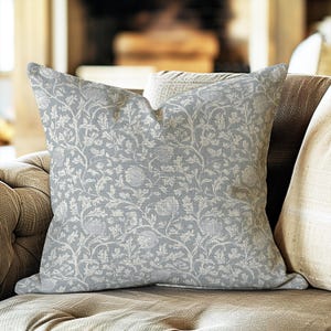 May include: A square throw cushion featuring a light grey fabric base with an intricate, repeating white botanical pattern of swirling vines, leaves, and rounded flower blossoms across the entire surface of the cushion cover.