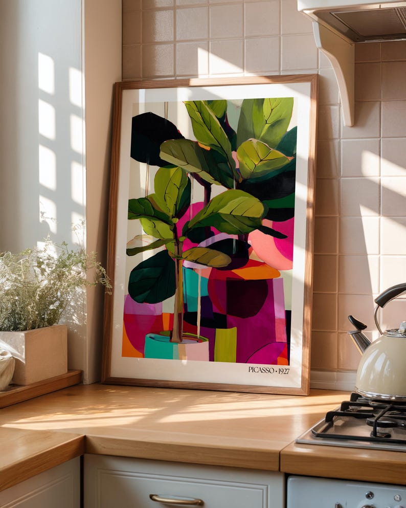 May include: A framed art print featuring a stylized fiddle leaf fig plant in a pot, rendered in vibrant shades of green, pink, purple, and orange. The composition includes abstract geometric shapes and the text PICASSO 1927 at the bottom center.