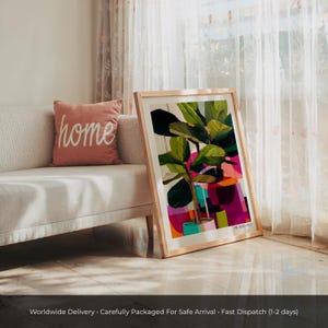 May include: A framed art print featuring a stylized illustration of a fiddle leaf fig plant in a pot. The artwork uses vibrant blocks of green, pink, purple, and orange. The print is housed in a light-colored wooden frame and rests on the floor.
