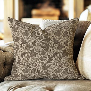 May include: A square throw pillow featuring a detailed, repeating botanical pattern in shades of dark brown and beige. The design consists of intricate illustrations of oak leaves and acorns covering the entire surface of the fabric cover.