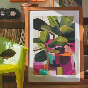 May include: A framed art print featuring a stylized fiddle leaf fig plant in a pot, set against a background of abstract geometric shapes in shades of pink, orange, and green. The print includes the text "PICASSO 1927" at the bottom right corner.