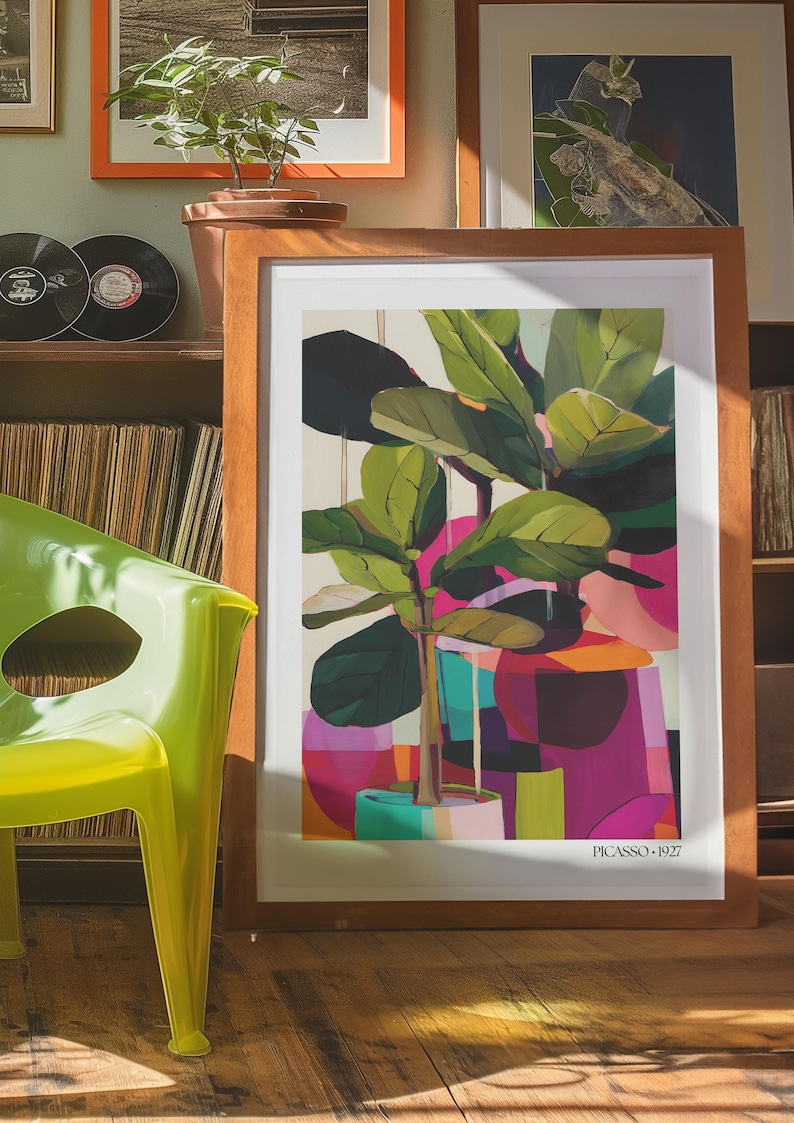 May include: A framed art print featuring a stylized fiddle leaf fig plant in a pot, set against a background of abstract geometric shapes in shades of pink, orange, and green. The print includes the text "PICASSO 1927" at the bottom right corner.