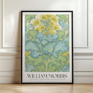 May include: A framed art print featuring a botanical illustration with blue-green cabbage-like leaves and yellow flowers on a cream background. The text WILLIAM MORRIS is printed in black at the bottom, followed by smaller text detailing the museum.