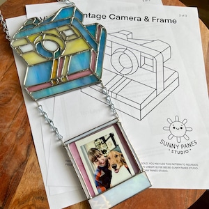 May include: A stained glass vintage camera and frame with a photo of a person and a dog. The camera is blue, yellow, and pink, and the frame is pink and white. The text "Vintage Camera & Frame" is visible.