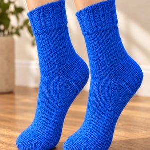 May include: A pair of vibrant royal blue hand-knitted socks featuring a thick ribbed cuff at the top and a classic stockinette stitch pattern throughout the foot and leg. The socks are crafted from a chunky yarn with a visible texture.