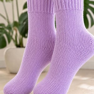 Puede incluir: Un par de calcetines de punto a media pantorrilla en un color lavanda claro sólido. Los calcetines presentan un puño acanalado en la parte superior y un patrón de punto jersey liso y consistente en todo el pie y la pierna.
