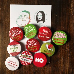 May include: A collection of ten 1.25 inch button badges with various Christmas-themed designs. The badges feature red, green, and white colours with text such as "Dear Santa", "Jingle Bells", "Ho Ho Ho", and "Merry Christmas".