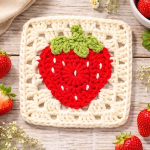 May include: A square, cream-colored crochet coaster with a red strawberry design. The strawberry has green leaves and white seed details. The coaster is surrounded by fresh strawberries on a wooden surface.