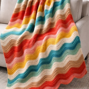 Puede incluir: Una manta de ganchillo hecha a mano, multicolor, con un diseño de rayas onduladas. La manta presenta una vibrante gama de colores, incluyendo rojo, naranja, amarillo, turquesa y beige. La manta está sobre un sofá gris.