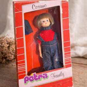 Puede incluir: Muñeca vintage llamada "Cosimo" en su caja original. La muñeca tiene cabello rubio, ojos azules y viste una camisa roja y un peto vaquero. La caja es roja con el logo "Petra Family".