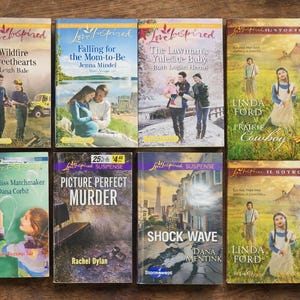 May include: A collection of eight paperback books with colorful covers. Titles include "Wildfire Sweethearts," "Falling for the Mom-to-Be," and "Picture Perfect Murder." The books are arranged on a wooden surface with green foliage.