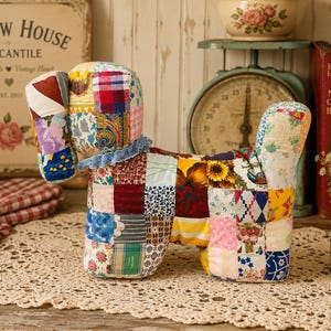 May include: A stuffed dog toy constructed from a patchwork of various colorful fabric squares featuring floral, plaid, and geometric patterns. The toy has a blue ruffled collar around its neck and is shaped like a standing canine with a raised tail.