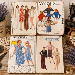 May include: Four vintage sewing pattern envelopes from McCall's, Butterick, and Simplicity brands. The paper envelopes feature illustrations of various clothing styles including dresses, tops, pants, and shorts, with printed brand names and pattern numbers.