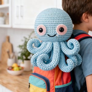 May include: A crocheted octopus toy in light blue, attached to a colourful backpack. The octopus has pink and black eyes and curly tentacles. The backpack is red, orange, yellow, and blue.