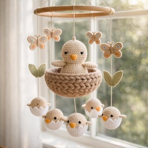 May include: A handmade crochet baby mobile featuring a chick in a nest, butterflies, and baby chicks hatching from eggs. The mobile is suspended from a wooden ring. The color palette includes beige, white, and light brown.