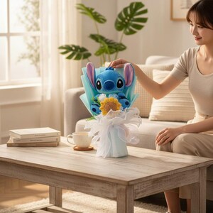 May include: A blue Stitch plush toy bouquet with a yellow sunflower and blue accents. The bouquet is wrapped in light blue paper and white ribbon, sitting on a wooden table. A woman is seen in the background.