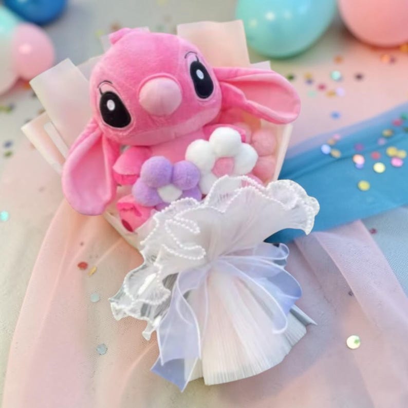 Puede incluir: Un ramo de peluche rosa con forma de personaje de dibujos animados, adornado con flores de tela blancas y moradas. El conjunto est&aacute; envuelto en encaje blanco y cintas transparentes. El fondo es pastel y salpicado de confeti.