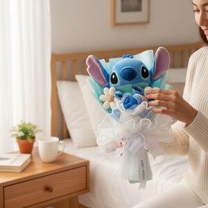 Peut inclure: Un bouquet de personnage Stitch en peluche bleue avec des accents bleu clair et blancs. Le bouquet comprend des fleurs en tissu et est envelopp&eacute; de papier bleu clair et de dentelle blanche. Un ruban blanc et le texte "LOVELY BLOOMS" compl&egrave;tent le tout.