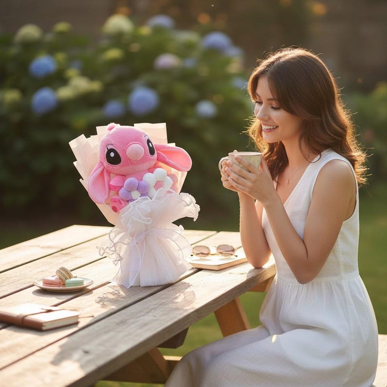 Puede incluir: Un ramo de peluche rosa con un personaje de orejas grandes y nariz redonda, envuelto en papel rosa y blanco con un lazo de tul blanco. El ramo est&aacute; sobre una mesa de picnic de madera.