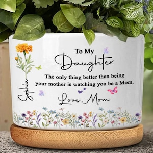 May include: White ceramic planter with a floral design at the base and the text "To My Daughter." The planter has a wooden base and features a marigold flower illustration and the name "Sophia."