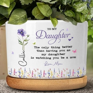May include: White ceramic planter with a wooden base, featuring floral and butterfly accents. Text reads "TO MY Daughter" and a personalized name. The message continues, "The only thing better than having you as my daughter is watching you be a mom. Love, Mom."