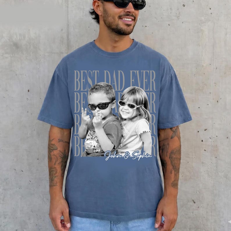 May include: Blue t-shirt with a graphic that says "BEST DAD EVER" in a repeating pattern. The graphic includes a black and white photo of two children wearing sunglasses. The names "John & Sophia" are written below the photo.
