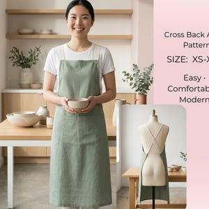 May include: A woman wearing a sage green cross-back apron with a white t-shirt. The apron has two front pockets and is labeled "Easy, Comfortable, Modern." The apron is available in sizes XS-XXL.