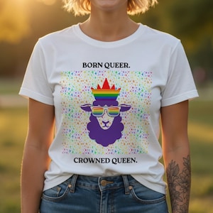May include: White t-shirt featuring a purple sheep wearing sunglasses and a rainbow crown. The text "BORN QUEER. CROWNED QUEEN." is printed above and below the graphic. The background is a pattern of colourful dots.