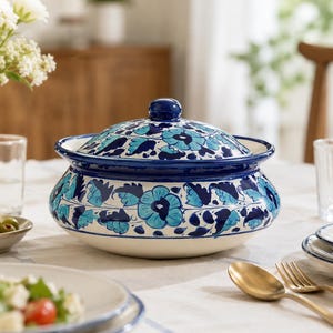 Puede incluir: Un cuenco de cerámica redondo con tapa a juego, decorado con un patrón floral pintado a mano en tonos azul oscuro y azul claro sobre un fondo blanco. El cuenco tiene un cuerpo ancho y curvo con un pequeño pomo en el centro de la tapa.