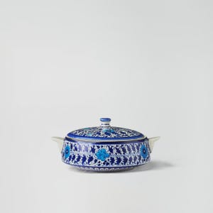 Puede incluir: Un cuenco de cerámica azul y blanco con tapa, adornado con un estampado floral. El cuenco tiene dos asas pequeñas y un pomo en la tapa. El diseño incluye flores y hojas estilizadas.