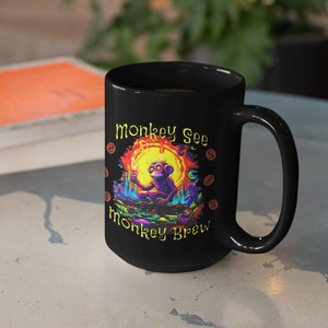 May include: Black ceramic mug featuring a colorful illustration of a monkey holding a lit object in front of a yellow sun. The mug has the text "Monkey See Monkey Brew" in yellow and orange.