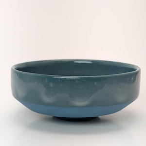 Puede incluir: Un cuenco de cerámica azul verdoso y azul. La parte superior del cuenco es azul verdoso, mientras que la base es de un tono azul más claro. El cuenco tiene un diseño sencillo y moderno, adecuado para servir alimentos o como pieza decorativa. Diámetro aproximado de 20 cm.