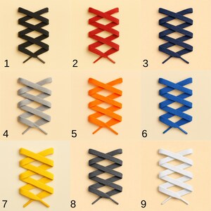 May include: Nine pairs of shoelaces in various colors, arranged in a grid. Colors include black, red, navy blue, gray, orange, blue, yellow, dark gray, and white. Each pair is laced in a crisscross pattern, showcasing the different color options.