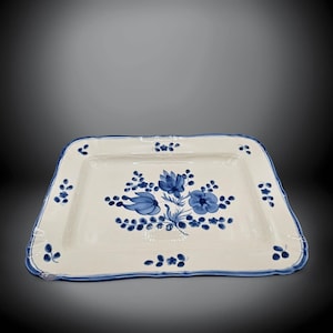 May include: Rectangular ceramic serving tray with a cream-colored base and a blue floral design. The tray has a scalloped edge with a blue border and is decorated with blue flowers and leaves. The tray is suitable for serving food.