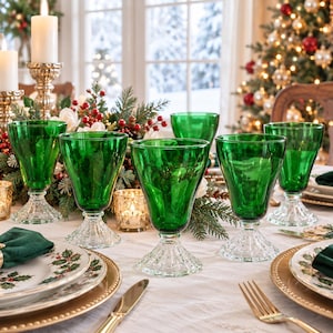 May include: A set of emerald green glass goblets with clear, textured, faceted bases. Each goblet features a smooth, deep green bowl and a sturdy, decorative stem that catches the light, arranged on a table setting with plates and cutlery.