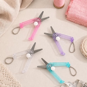 Peut inclure: Quatre petits coupe-fils à ressort avec des poignées en plastique translucide rose, violet, transparent et bleu sarcelle. Chaque outil possède une lame en métal, un pivot circulaire blanc et une chaînette à billes argentée gravée.